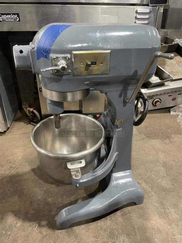 Hobart commercial electric planetary mixer with mixing bowl, heavy-duty, mounted on legs. Steel body, visible wear.