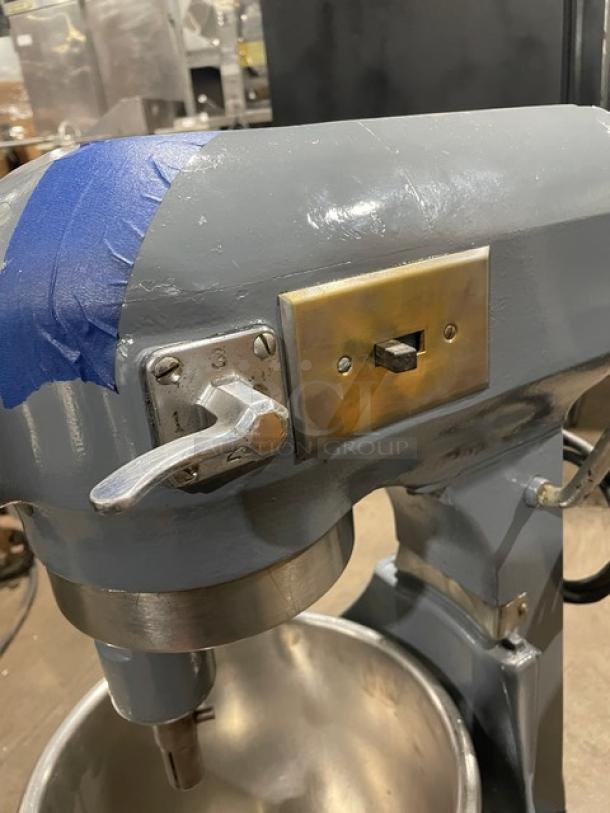 Hobart commercial electric planetary mixer with mixing bowl and legs, shown in used condition. Features control lever and brass panel.
