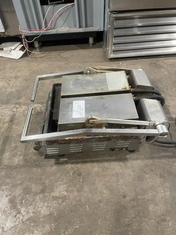 Commercial stainless steel electric countertop dual panini press grill, with legs. Shows wear and a visible tag.