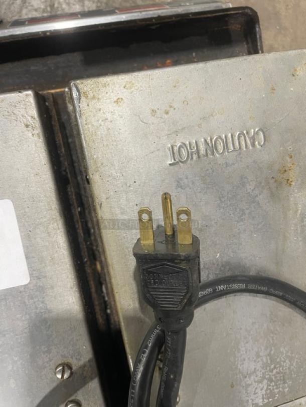 Commercial stainless steel electric dual panini press grill, countertop model, visible "CAUTION HOT" marking, plugged cord shown.