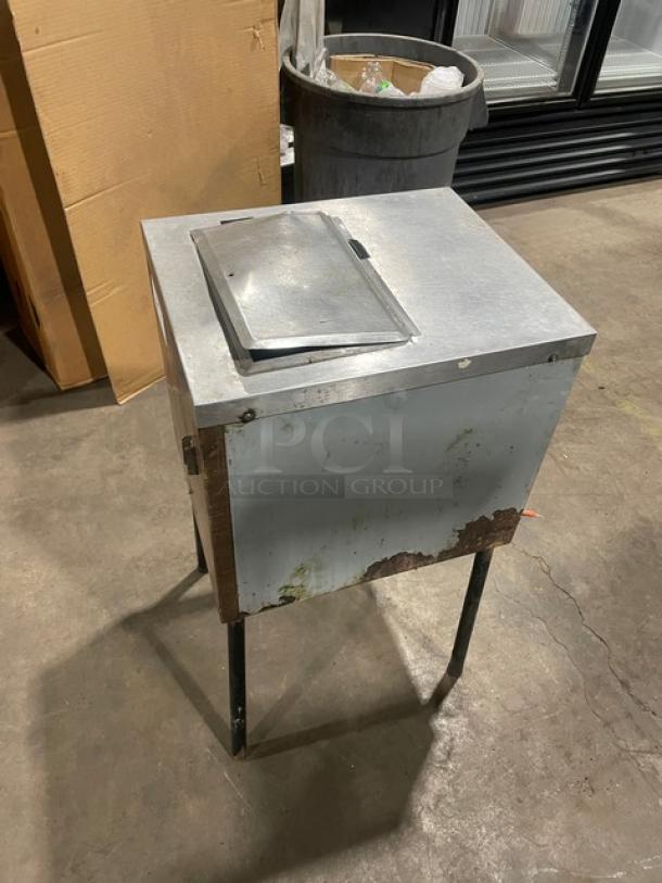 Commercial ice crushing machine with stainless steel top, wooden style sides, mounted on legs. Visible wear and rustic appearance.