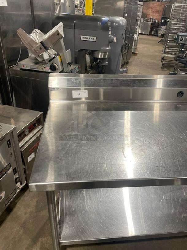 Commercial stainless steel prep table with single undershelf and up-turned backsplash, on casters, showing minor surface wear.