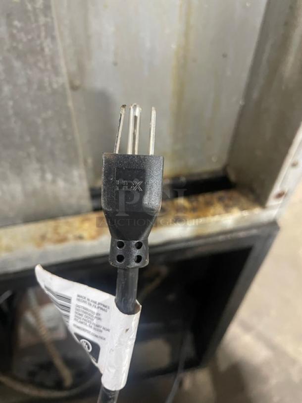 Close-up of a three-prong plug with a tag indicating "HDX" branding. The background shows part of a Blodgett stainless steel oven.