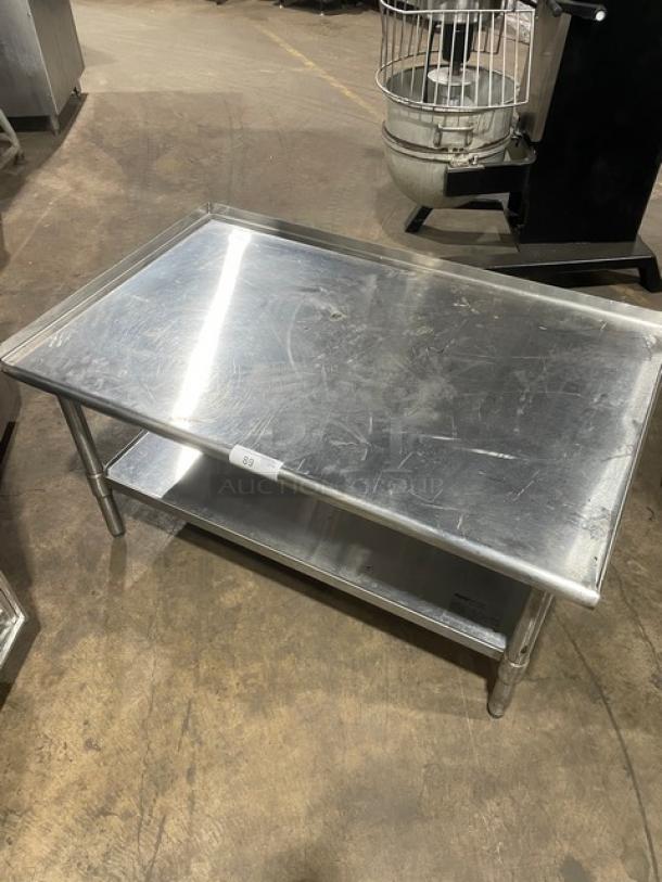 Commercial stainless steel food prep table with under-shelf and legs, showing signs of wear. Ideal for kitchen use.