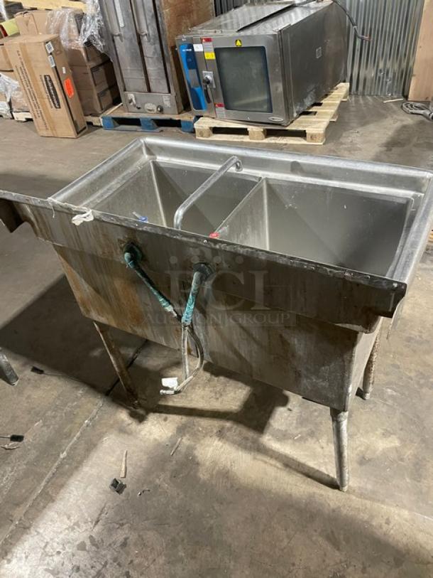 All stainless steel 2-compartment dishwashing/prep sink with faucet and legs. Industrial-grade. Visible wear and connections.