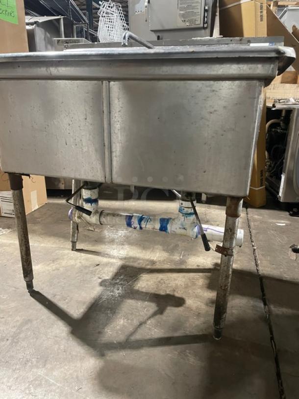 All stainless steel 2 compartment dishwashing/prep sink with faucet and legs. Industrial design, visible piping.