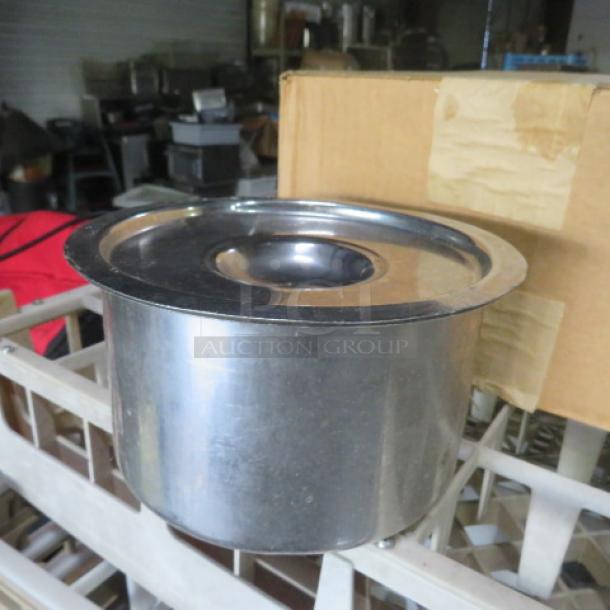 Stainless steel crock with lid, shiny finish, likely in used condition, lid fits securely, visible in storage area.
