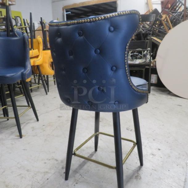 Vintage-style blue bar stool with cushioned swivel seat, tufted back, nailhead trim, and gold footrest.