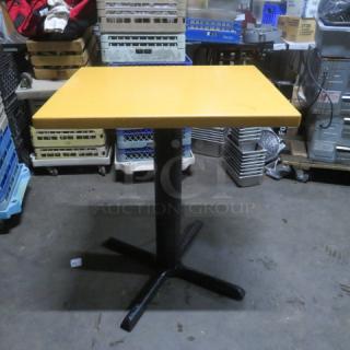 Yellow solid wooden table on bar height pedestal base, 24x30x35.5 inches. Black metal base, good condition.