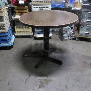 Round wooden tabletop on bar-height pedestal base, 36x42 inches. Features a cross-shaped metal base. Used condition.