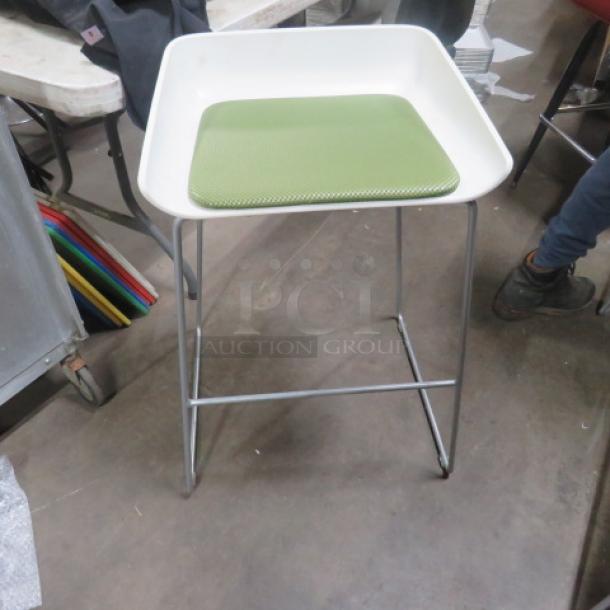 Metal stool with a green cushioned seat, featuring a minimalist design and sturdy metal legs. Appears in good condition.