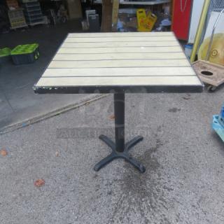 Bar-height patio table, 30x30x36 inches, wood-like slat top, black metal base, signs of wear, ideal for outdoor use.