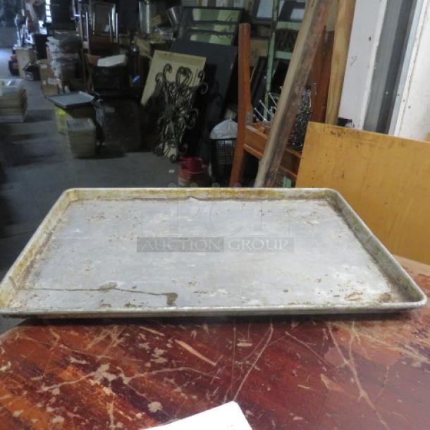 Full-size sheet pan, used, metal surface with visible wear and discoloration, model 5XBID, resting on a wooden table.