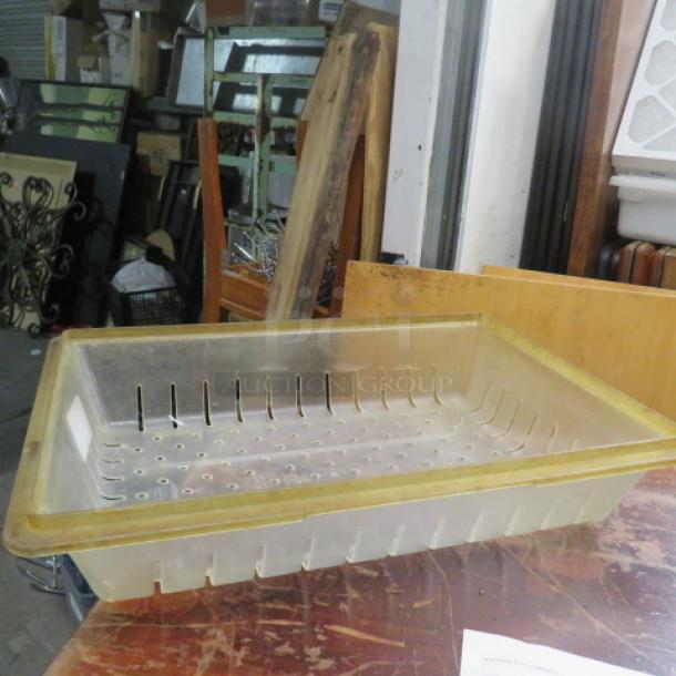 Transparent 8.75-gallon perforated food storage container, slightly worn, with a yellow rim, on a wooden surface.