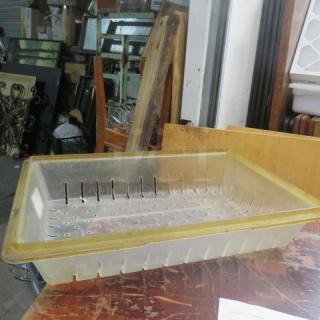 Transparent 8.75-gallon perforated food storage container, slightly worn, with a yellow rim, on a wooden surface.