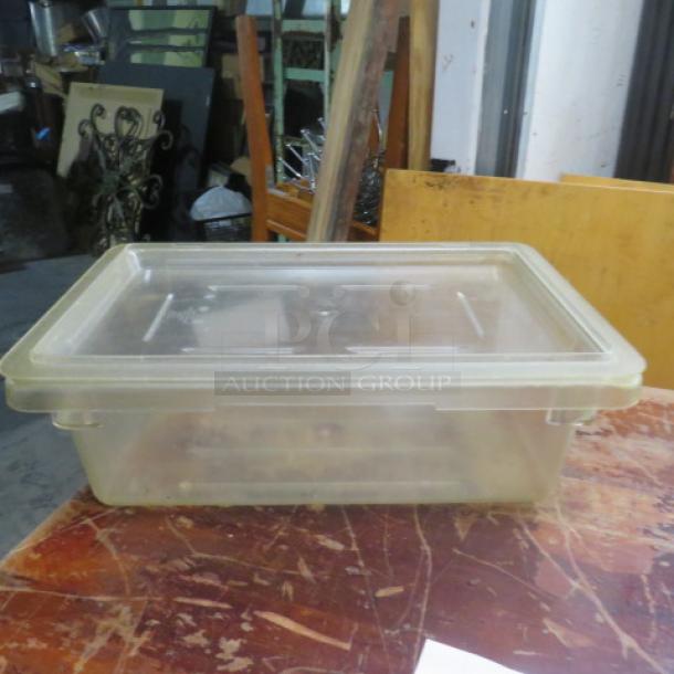 Clear 3-gallon food storage container with lid, rectangular shape, used condition, visible scuffs, set on wooden surface.