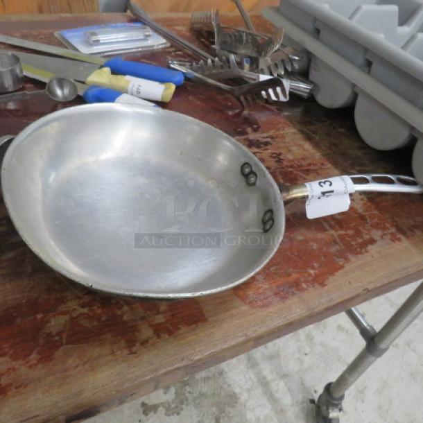 10-inch sauté pan with a riveted handle, silver tone, lightly worn condition, placed on a wooden surface.