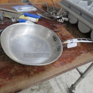 10-inch sauté pan with a riveted handle, silver tone, lightly worn condition, placed on a wooden surface.