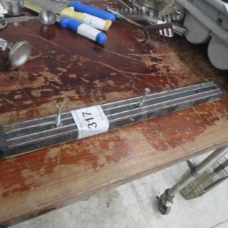 Magnetic knife holder with black finish, mounted screws, and auction label numbered 317, on a wooden table.