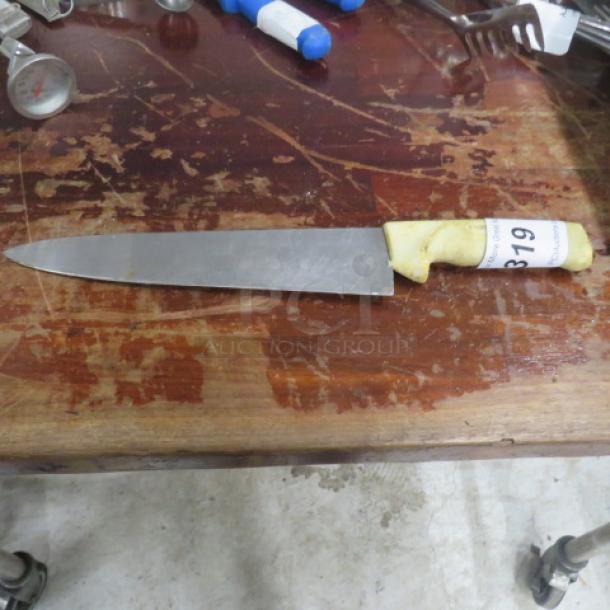 Chef knife with stainless steel blade, white handle, visible wear, auction tag labeled "319," on wooden surface.