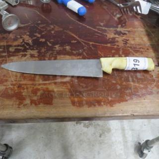 Chef knife with stainless steel blade, white handle, visible wear, auction tag labeled "319," on wooden surface.