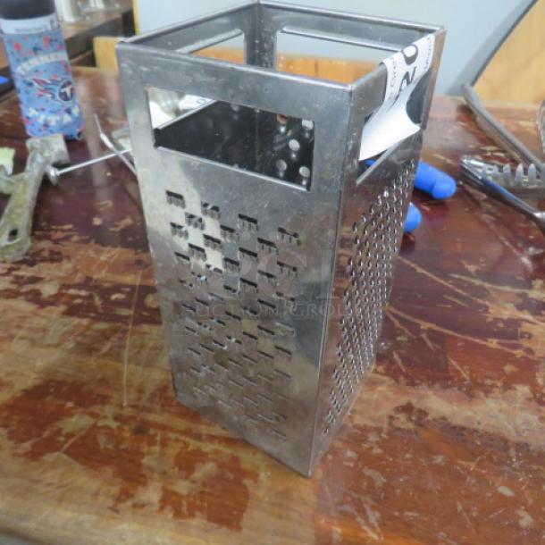 Stainless steel box grater with multi-sized grating surfaces, in good condition, showing minor wear.