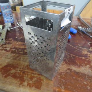 Stainless steel box grater with multi-sized grating surfaces, in good condition, showing minor wear.
