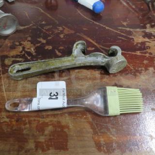 Lot of assorted utensils with a vintage metal bottle opener and a silicone basting brush on a wooden surface. Auction tag 31.