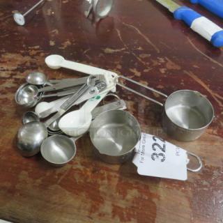 Assorted measuring cups and spoons on wood surface, varying sizes, metal and plastic. Includes auction tag numbered 322.