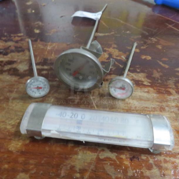 Assorted thermometers on wooden surface; includes dial and tube types, metal construction, mixed condition, visible wear.