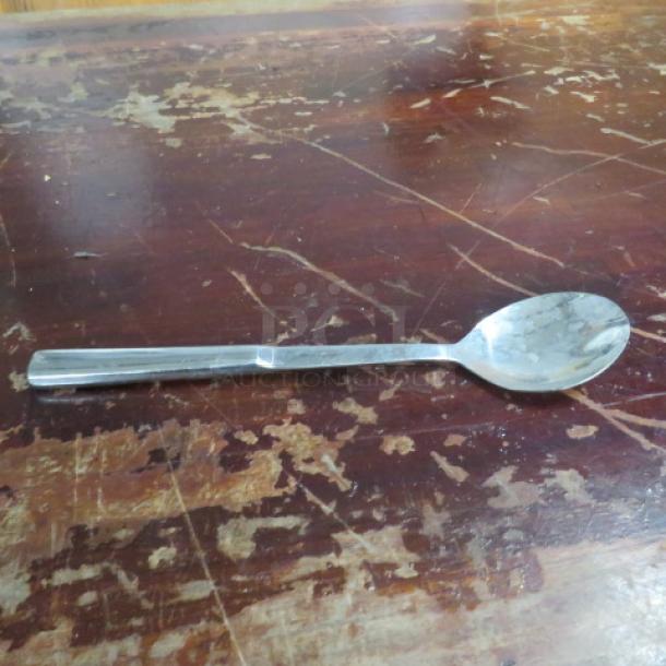Stainless steel spoon on a worn wooden surface; simple design, reflective finish, good condition. No visible markings.