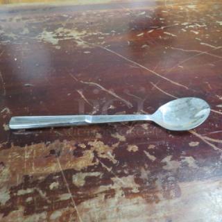Stainless steel spoon on a worn wooden surface; simple design, reflective finish, good condition. No visible markings.