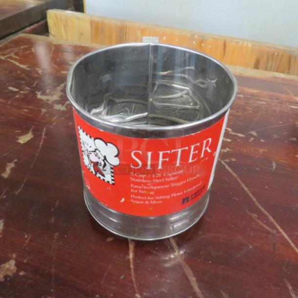 NEW stainless steel sifter with red label, 5-cup capacity, spring-action handle, ideal for sifting flour and sugar.