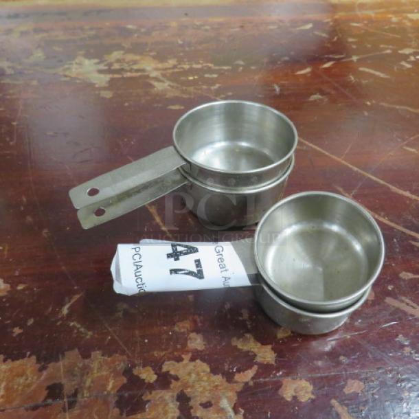Stacked stainless steel measuring cups on a worn wooden table, auction tag number 47 visible.