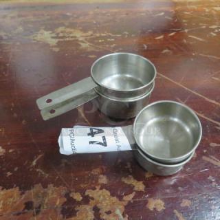 Stacked stainless steel measuring cups on a worn wooden table, auction tag number 47 visible.