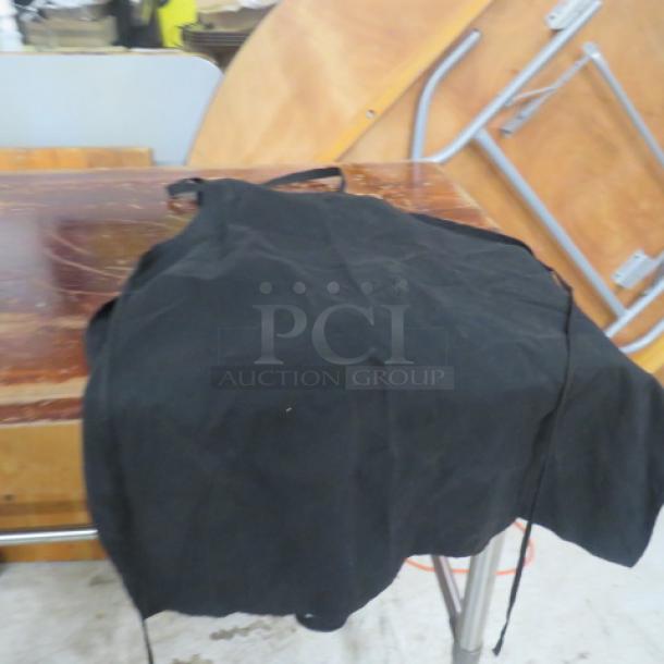 Black apron displayed on a wooden surface, highlights simple design and durable fabric, suitable for kitchen or workshop use.