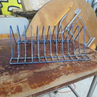 Blue metal one pan rack with multiple vertical slots for organizing. Shows wear and rust on a wooden surface.