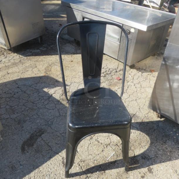 Black metal chair with curved backrest and simple design. Slight wear visible. Suitable for industrial or modern decor.