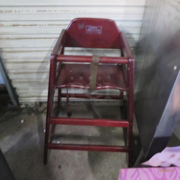 Wooden high chair with safety straps, red finish, visible manufacturer's label, sturdy condition. Ideal for auctions.