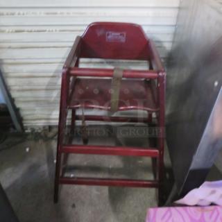 Wooden high chair with safety straps, red finish, visible manufacturer's label, sturdy condition. Ideal for auctions.