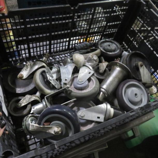 A plastic crate filled with assorted industrial casters, various sizes and types, metal and rubber, used condition.