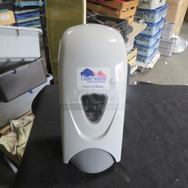 Wall mount soap dispenser, brand "Cleaner Solutions," model "Foam-O-Matic," new condition, sleek white design, visible label.