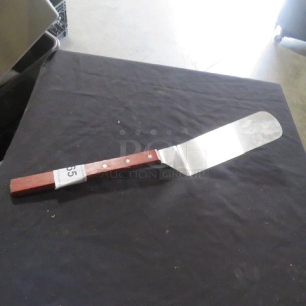 Metal hamburger turner with a wooden handle and three rivets, showing moderate wear. Auction tag labeled “65.”