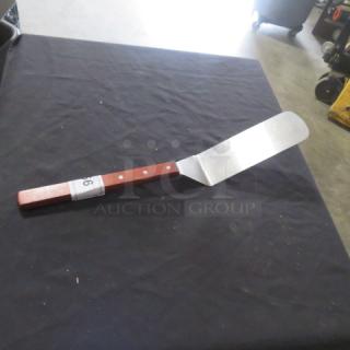 A stainless steel hamburger turner with a wooden handle, in good condition, displayed on a dark fabric surface.