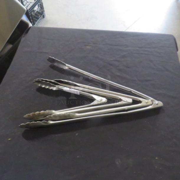Assorted stainless steel tongs on table, scissor style, silver finish, slightly used condition, ideal for kitchen use.