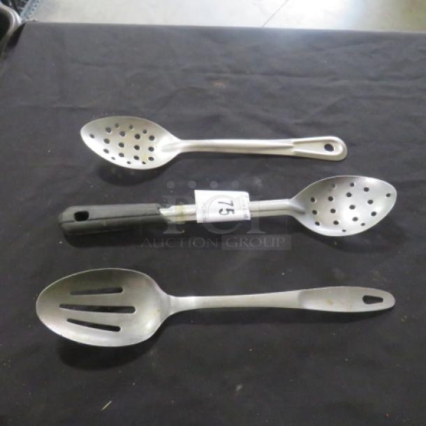 Assorted stainless steel slotted spoons, set of three, with varied handle designs; tag labeled "75" visible on one spoon.