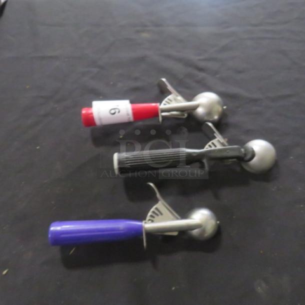 Three assorted dishers with red, black, and blue handles on black surface. Numbered tag "16" on red disher.