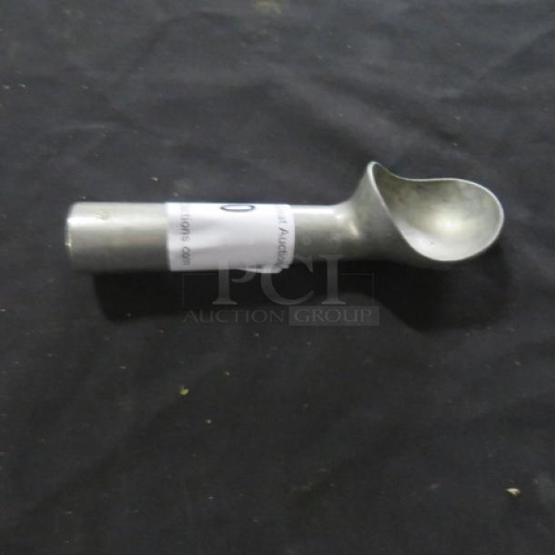 Stainless steel ice cream scoop with cylindrical handle, intact condition, featuring a small tag wrapped around the handle.