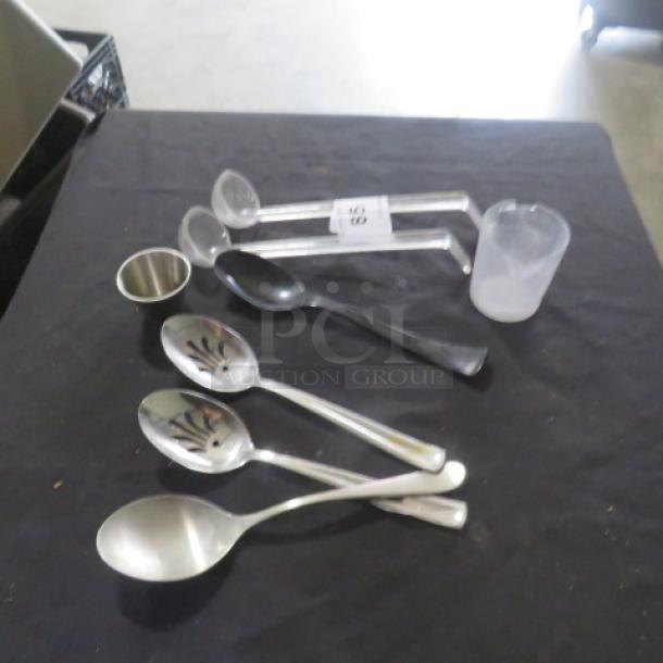 A lot of miscellaneous kitchen utensils on a black surface, including measuring cups and metal and plastic spoons. Items vary in condition.