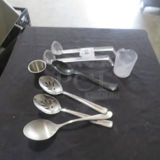 A lot of miscellaneous kitchen utensils on a black surface, including measuring cups and metal and plastic spoons. Items vary in condition.